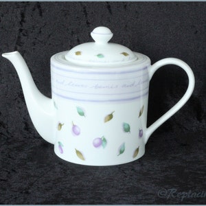 May include: White teapot with a purple and green floral design. The teapot has a lid and a handle. The text on the teapot reads "And leaves berries and blooms".