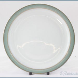 Puede incluir: Un plato de cerámica blanco con un borde verde claro y un ribete dorado. El plato es redondo y tiene un diseño simple y elegante. El plato es probablemente para servir comida.