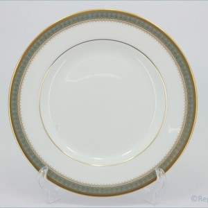 Puede incluir: Un plato de cena de porcelana blanca con un borde dorado y verde. El borde presenta un patrón repetitivo de hojas y flores estilizadas.