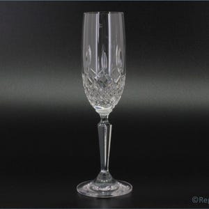 Op de afbeelding: Een heldere glazen champagnefluit met een geslepen kristallen ontwerp. De fluit heeft een lange steel en een ronde voet.