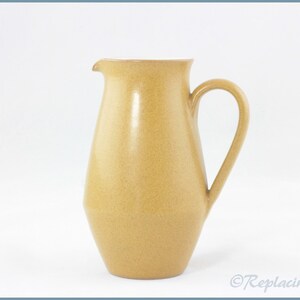 May include: A tan ceramic jug with a rounded body and a handle. The jug has a textured surface.