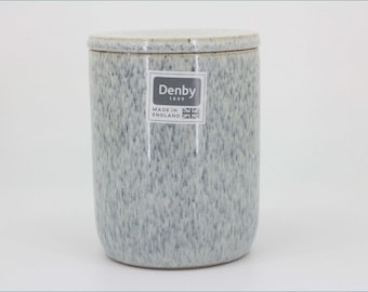 May include: A cylindrical ceramic storage canister with a speckled light gray and white glaze. The canister features a matching lid and a rectangular sticker on the front displaying the text Denby 1809 Made in England with a small Union Jack flag icon.