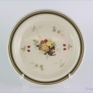 May include: A white ceramic dinner plate with a brown rim and a floral design featuring fruit and berries. The plate has a speckled glaze.