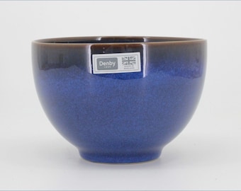 May include: A round ceramic bowl with a deep blue glaze that transitions to a dark brown rim. A rectangular sticker on the front features the text Denby 1809 and a small Union Jack flag with the words Made in England printed below the flag icon.