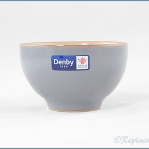 Puede incluir: Un cuenco de cerámica azul claro con un acabado liso y forma redondeada. Una pegatina azul rectangular está centrada en la parte frontal, con el texto blanco Denby 1809 y un pequeño icono de la Union Jack con Made in England.