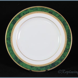 May include: A white dinner plate with a green and gold rim. The rim has a marbled green design with a gold trim.