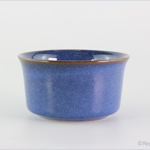 May include: A blue ceramic bowl with a speckled texture. The bowl has a rounded shape with a brown rim. The interior of the bowl is a darker shade of blue. The bowl is sitting on a white surface.