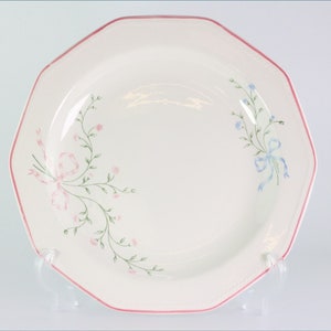 May include: A white octagonal dinner plate with a pink and blue floral design. The plate has a pink rim and a delicate floral pattern with bows.