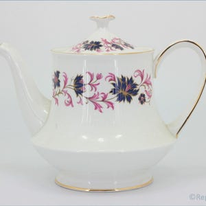 Peut inclure: Théière en porcelaine blanche avec couvercle, ornée d'un motif floral bleu marine et rose. La théière a une bordure dorée sur la poignée, la base et le couvercle. Une pièce classique pour servir le thé.