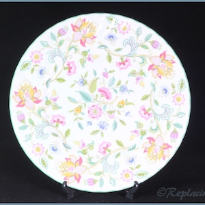 May include: A white ceramic dinner plate with a green rim and a floral pattern in shades of pink, yellow, and blue.