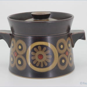 Może przedstawiać: Brązowa ceramiczna naczynie do zapiekania z pokrywką. Naczynie ma geometryczny wzór w odcieniach brązu, żółtego i czerwonego.