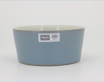 May include: A light blue ceramic bowl with a smooth matte finish and a white interior. A rectangular sticker on the front features the text Denby 1809, a small Union Jack flag icon, and the words Made in England in a clear, sans-serif font.