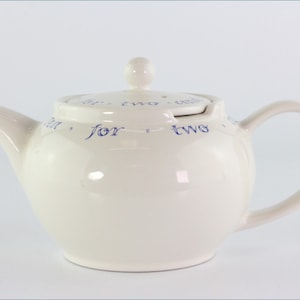 Könnte beinhalten: Weiße Teekanne aus Keramik mit einer blauen Aufschrift "Tee für zwei".