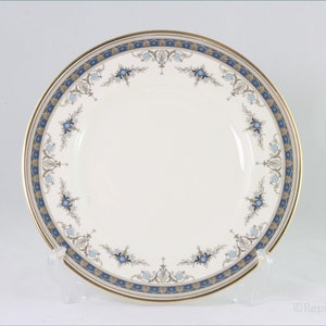May include: A white ceramic dinner plate with a blue and gold floral border. The plate has a gold rim and a delicate floral pattern.