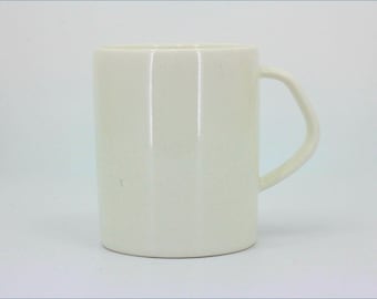 May include: A plain, off-white ceramic mug with a smooth, glossy finish. The mug features a cylindrical body and a single, angular handle attached to the side. The design is simple and functional, with no patterns, textures, or additional markings.