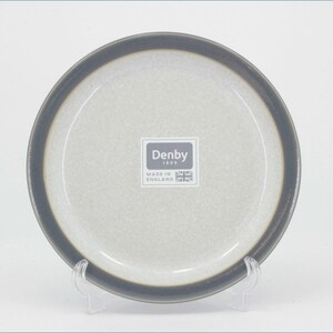 May include: A round ceramic plate with a speckled light grey centre and a dark charcoal grey rim. The centre features a white square label with the text Denby 1809 Made in England and a small Union Jack flag icon printed in dark grey ink.