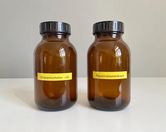 May include: Two amber glass bottles with black lids. One bottle has a yellow label that reads "Orangenschalen süß". The other bottle has a yellow label that reads "Passionsblumenkraut".
