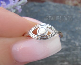 May include: Silver ring with an evil eye design. The ring is on a finger and the background is blurred.