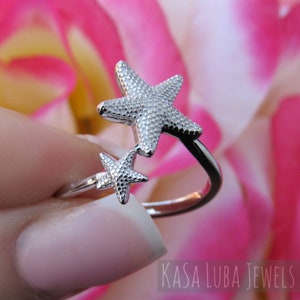 May include: A silver ring with two star-shaped designs. The ring is adjustable and has a textured finish.