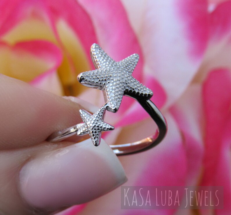 May include: A silver ring with two star-shaped designs. The ring is adjustable and has a textured finish.