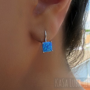 May include: Silver earrings with a square blue opal gemstone. The earrings are dangling and have a simple design.
