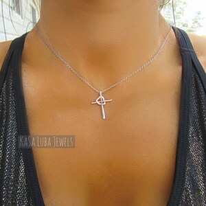 Puede incluir: Un collar de cadena de plata con un colgante de cruz de plata. La cruz tiene un peque&ntilde;o c&iacute;rculo en el centro.