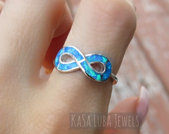 May include: A silver infinity ring with a blue opal inlay. The ring is on a finger.