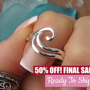 May include: Silver ring with a wave design. The ring is on a finger and the wave design is a double swirl.
