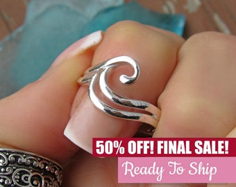 May include: Silver ring with a wave design. The ring is on a finger and the wave design is a double swirl.