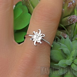 May include: A silver ring with a sun design. The sun has a face with a smile and rays extending out from it.