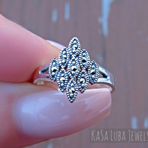May include: A silver ring with a geometric design made of marcasite stones. The ring is set on a finger.