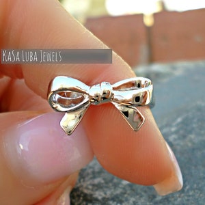May include: A silver bow ring. The ring is worn on a finger.