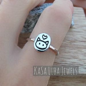 May include: A silver ring with a cat face design and a small heart above it. The ring is on a finger and the text "KASA LUBA JEWELS" is visible below the ring.