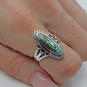 May include: A silver ring with an oval abalone shell inlay. The ring has a delicate filigree design around the shell.