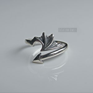 May include: A silver ring with a wing design. The ring is open and adjustable. The ring is made of sterling silver.