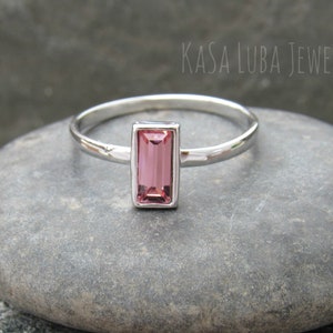 May include: A silver ring with a pink rectangular gemstone. The ring is on a gray stone background.