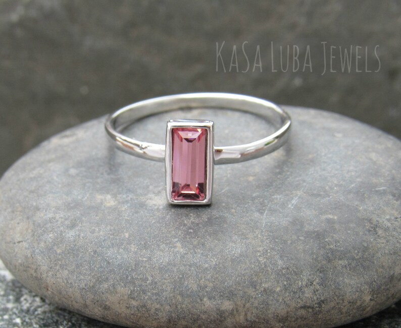 May include: A silver ring with a pink rectangular gemstone. The ring is on a gray stone background.