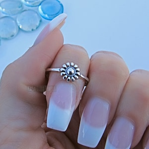 May include: A silver ring with a small daisy design. The ring is on a finger with white nail polish.