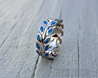 Könnte beinhalten: Ein silberner Ring mit einem blauen Opal-Blattdesign. Der Ring liegt auf einem hellen Holzuntergrund.