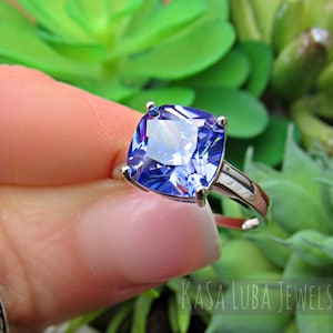 May include: A silver ring with a large, square-shaped, blue gemstone. The gemstone has a faceted cut and a light blue color.