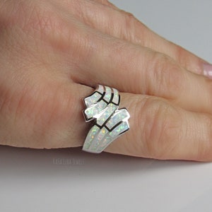 Op de afbeelding: Een zilveren ring met een ontwerp van witte opaal. De ring wordt gedragen aan een vinger.