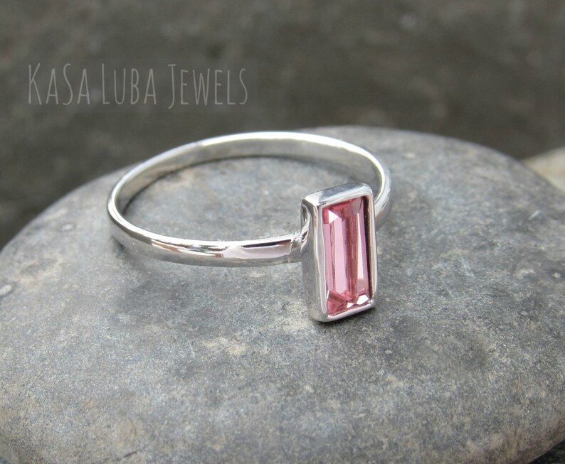 May include: A silver ring with a pink rectangular gemstone. The ring is on a gray stone surface.