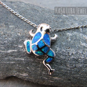 May include: A silver chain necklace with a blue opal frog pendant. The frog is facing away from the viewer and has a detailed design.