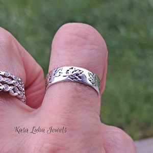 May include: A silver ring with a leaf design. The ring is on a finger.