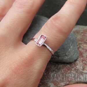 May include: A delicate silver ring with a pink rectangular gemstone set in a bezel setting. The ring band is textured with a hammered finish.