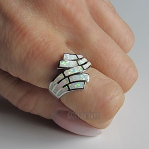 Op de afbeelding: Een zilveren ring met een witte opaal-steen gezet in een geometrisch ontwerp. De ring wordt gedragen aan een vinger.