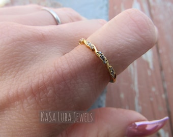 May include: A gold band ring with a twisted design and small clear stones. The ring is on a finger.