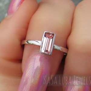May include: A silver ring with a rectangular pink gemstone. The ring is on a finger with pink nail polish.