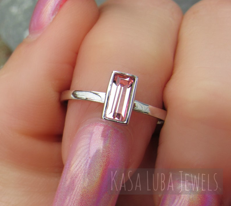 May include: A silver ring with a rectangular pink gemstone. The ring is on a finger with pink nail polish.