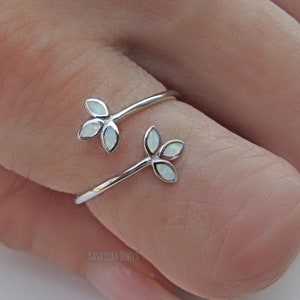 May include: A silver ring with two delicate branches adorned with white opal stones. The ring is designed to be worn on the thumb or finger.